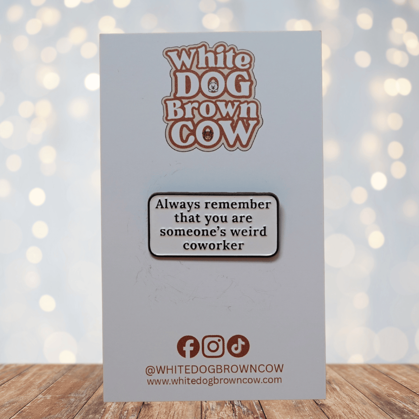 Rectangular enamel pin with the quote “Always remember that you are someone’s weird coworker” in black text on a white background.