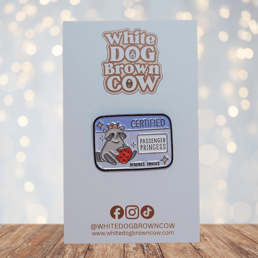 Raccoon enamel pin wearing a crown, holding a strawberry, with text “Certified Passenger Princess – Requires Snacks.”