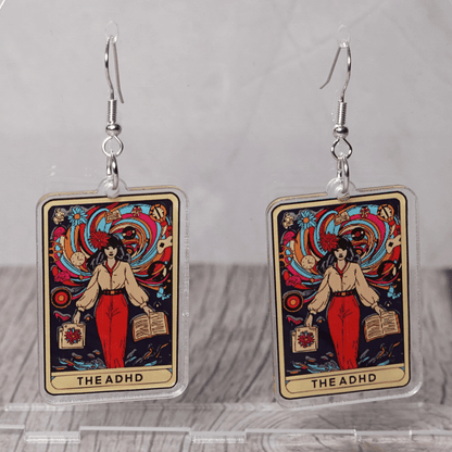 Acrylic dangle earrings featuring a colorful tarot-style card labeled “The ADHD” with a woman surrounded by swirling patterns and books.