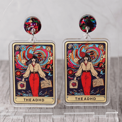 Acrylic dangle earrings featuring a colorful tarot-style card labeled “The ADHD” with a woman surrounded by swirling patterns and books.