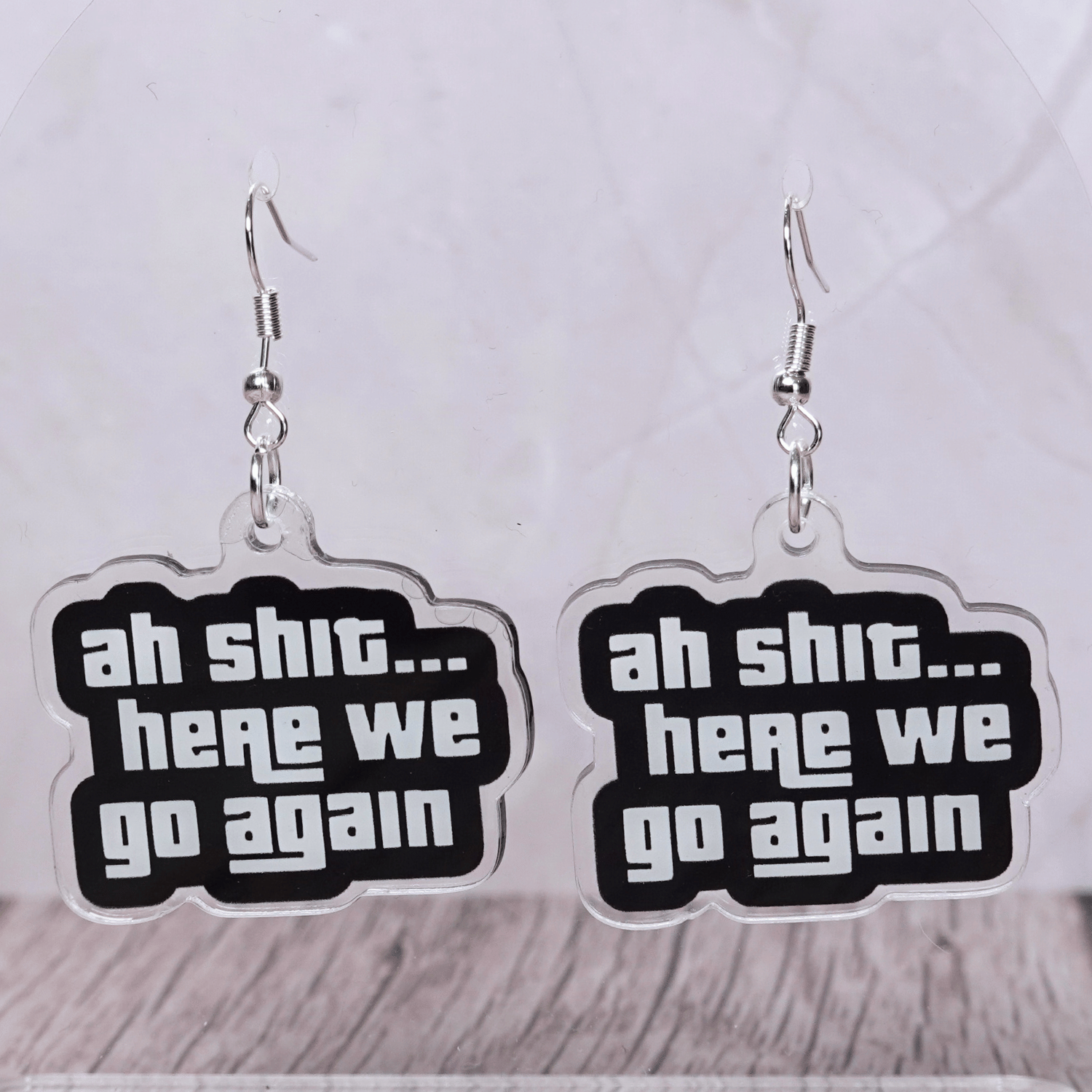 Black and white novelty earrings with text “ah shit here we go again”