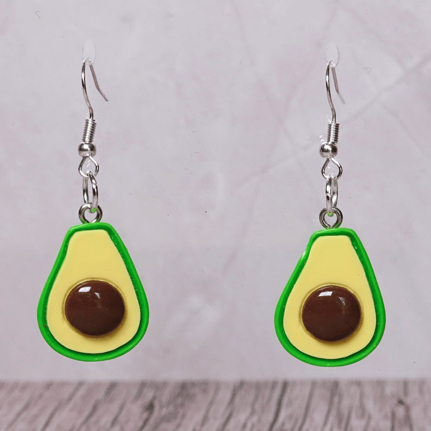 Avocado shaped dangle earrings with green outline, pale yellow center and raised brown pit on silver hooks.