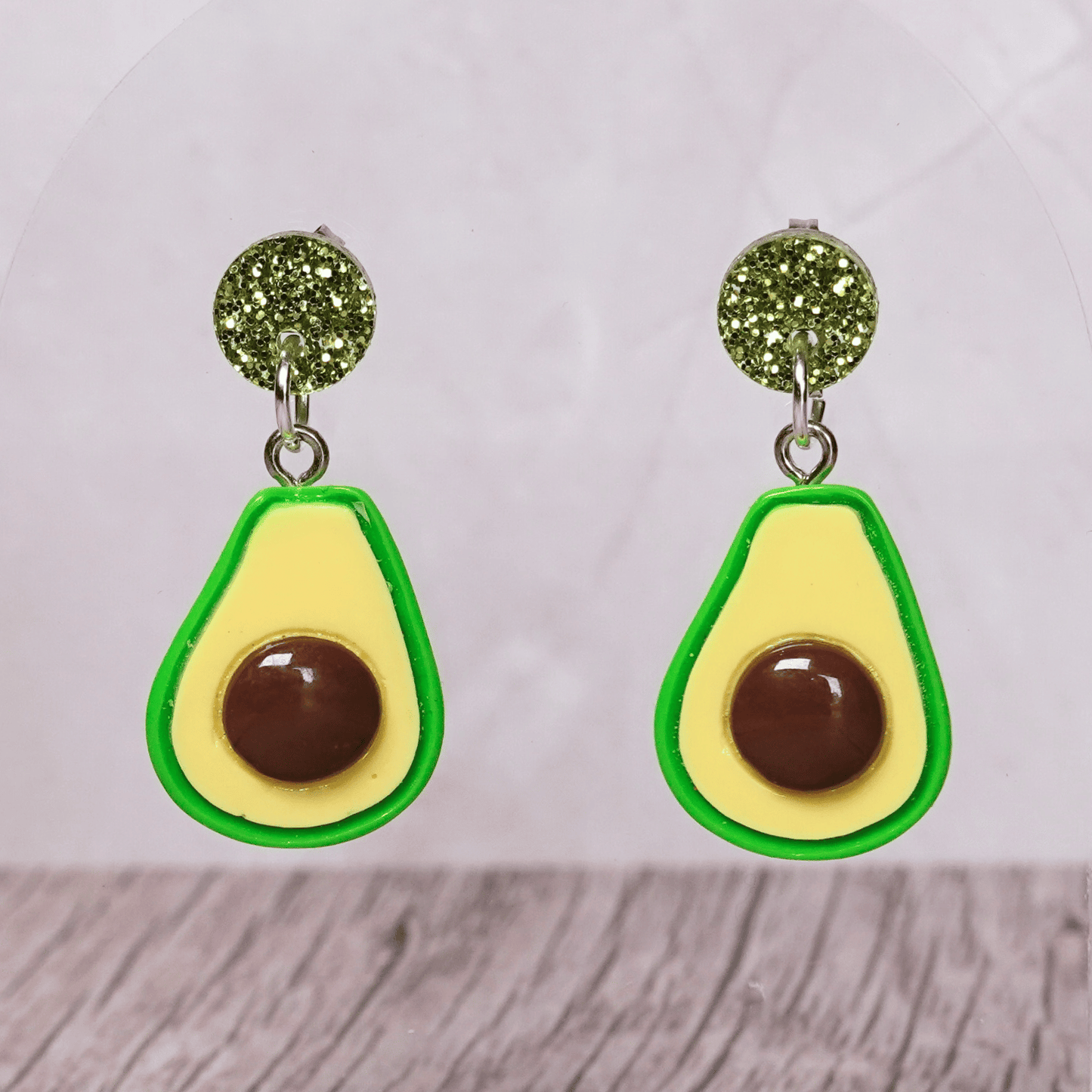 Avocado shaped dangle earrings with green outline, pale yellow center and raised brown pit on glitter studs