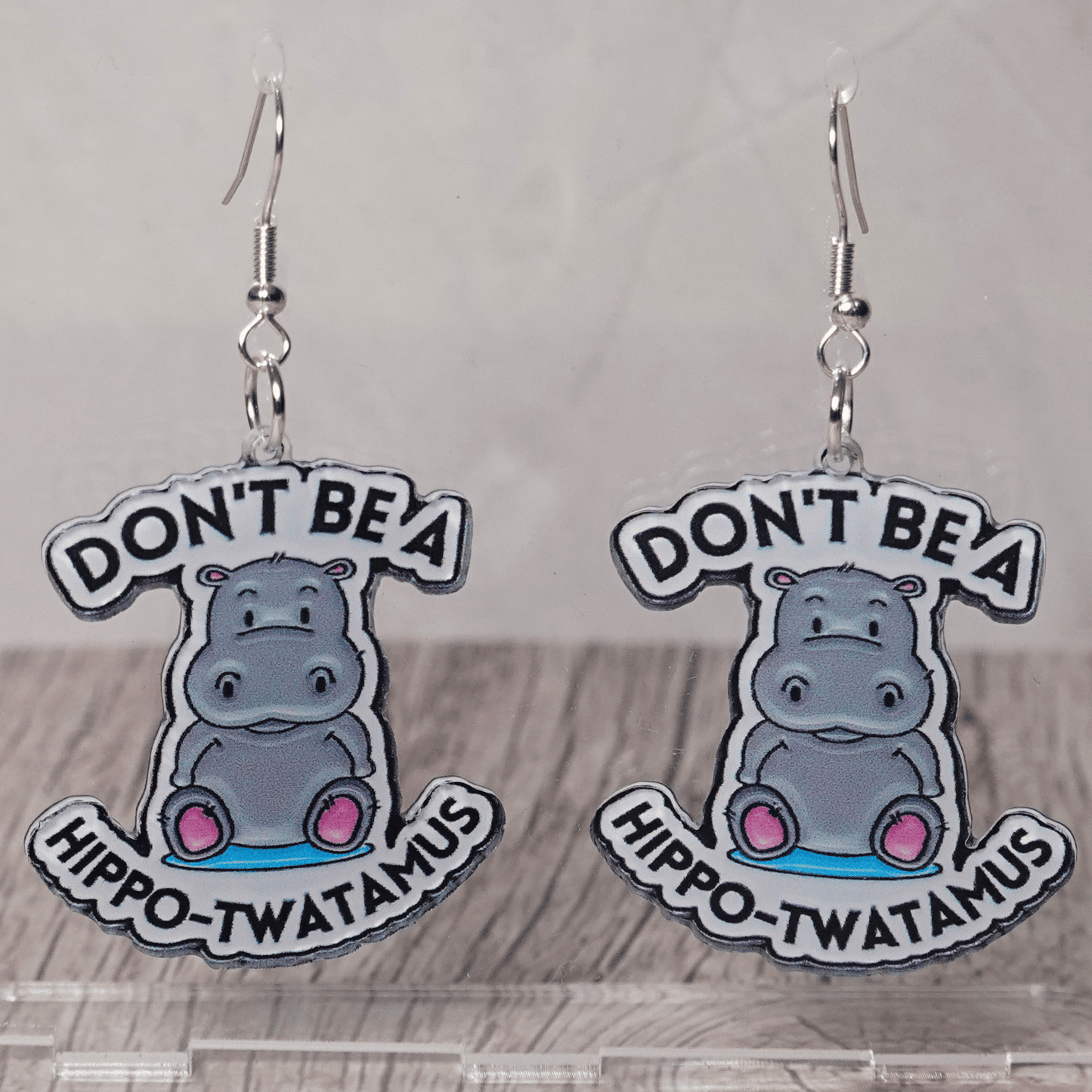 Novelty dangle earrings with a cute cartoon hippo and the phrase “Don’t be a hippo-twatamus”
