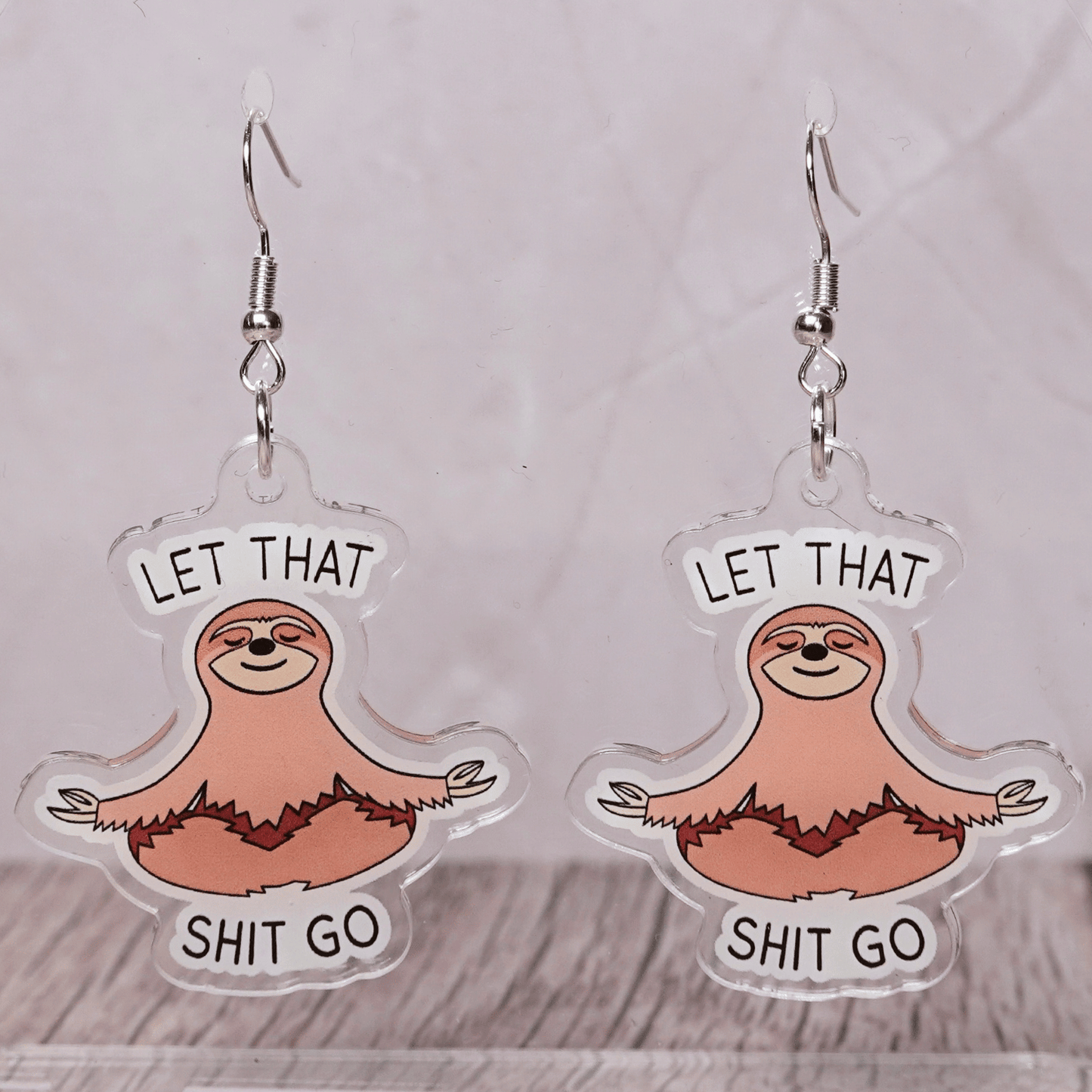 Cute sloth dangle earrings in meditation pose with text “let that shit go”