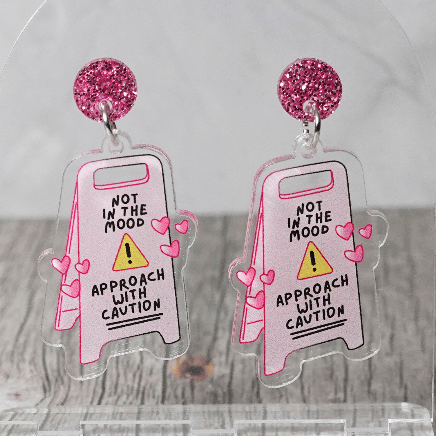 Funny acrylic dangle earrings shaped like a caution sign that reads “Not in the mood – approach with caution,” decorated with small pink hearts.