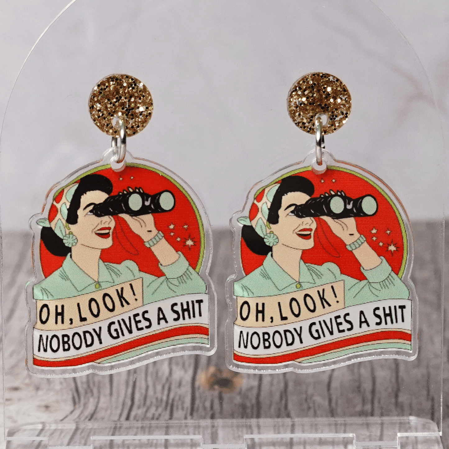Retro style novelty dangle earrings showing a woman with binoculars and the phrase “Oh look nobody gives a sh*t”