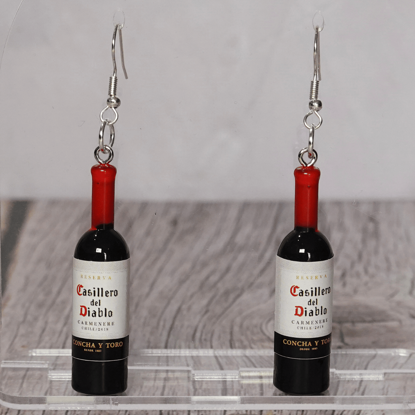 Mini red wine bottle shaped dangle earrings with silver hooks on display stand.