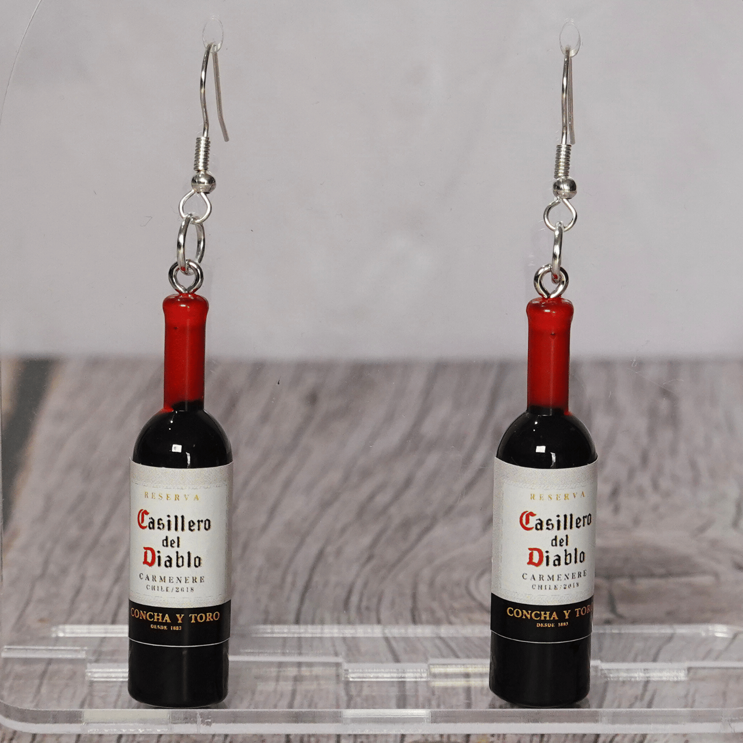 Mini red wine bottle shaped dangle earrings with silver hooks on display stand.