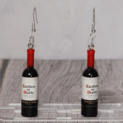 Mini red wine bottle shaped dangle earrings with silver hooks on display stand.