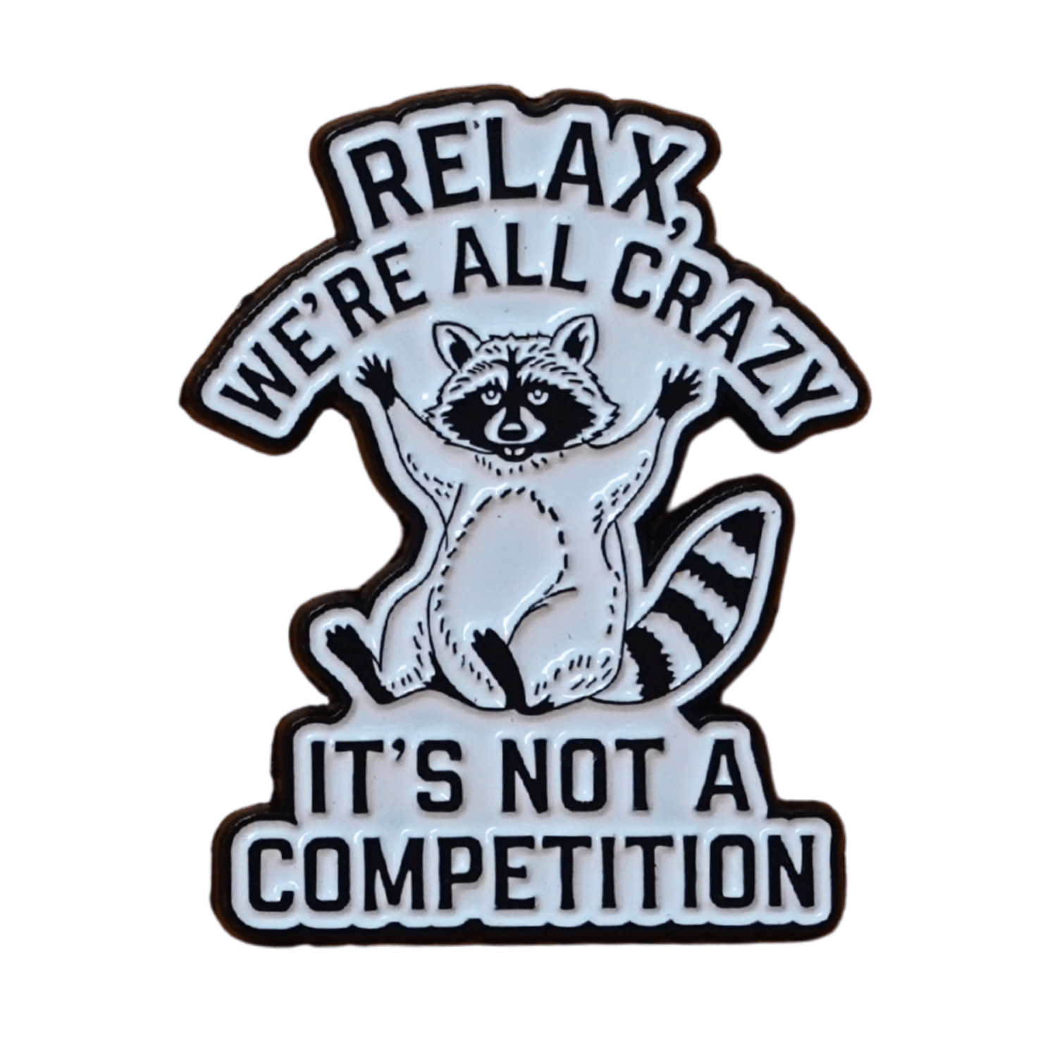 Black and white enamel pin with raccoon illustration and quote “Relax, We’re All Crazy, It’s Not a Competition,” funny sarcastic lapel pin.