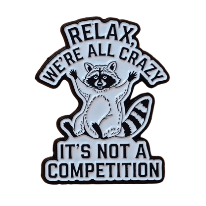 Black and white enamel pin with raccoon illustration and quote “Relax, We’re All Crazy, It’s Not a Competition,” funny sarcastic lapel pin.