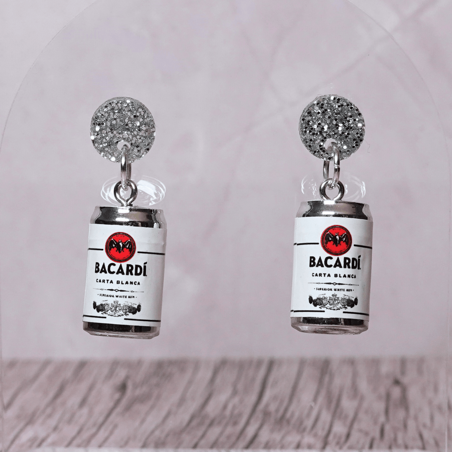 Novelty dangle earrings shaped like mini bacardi white rum cans with a printed label design and silver glitter studs.