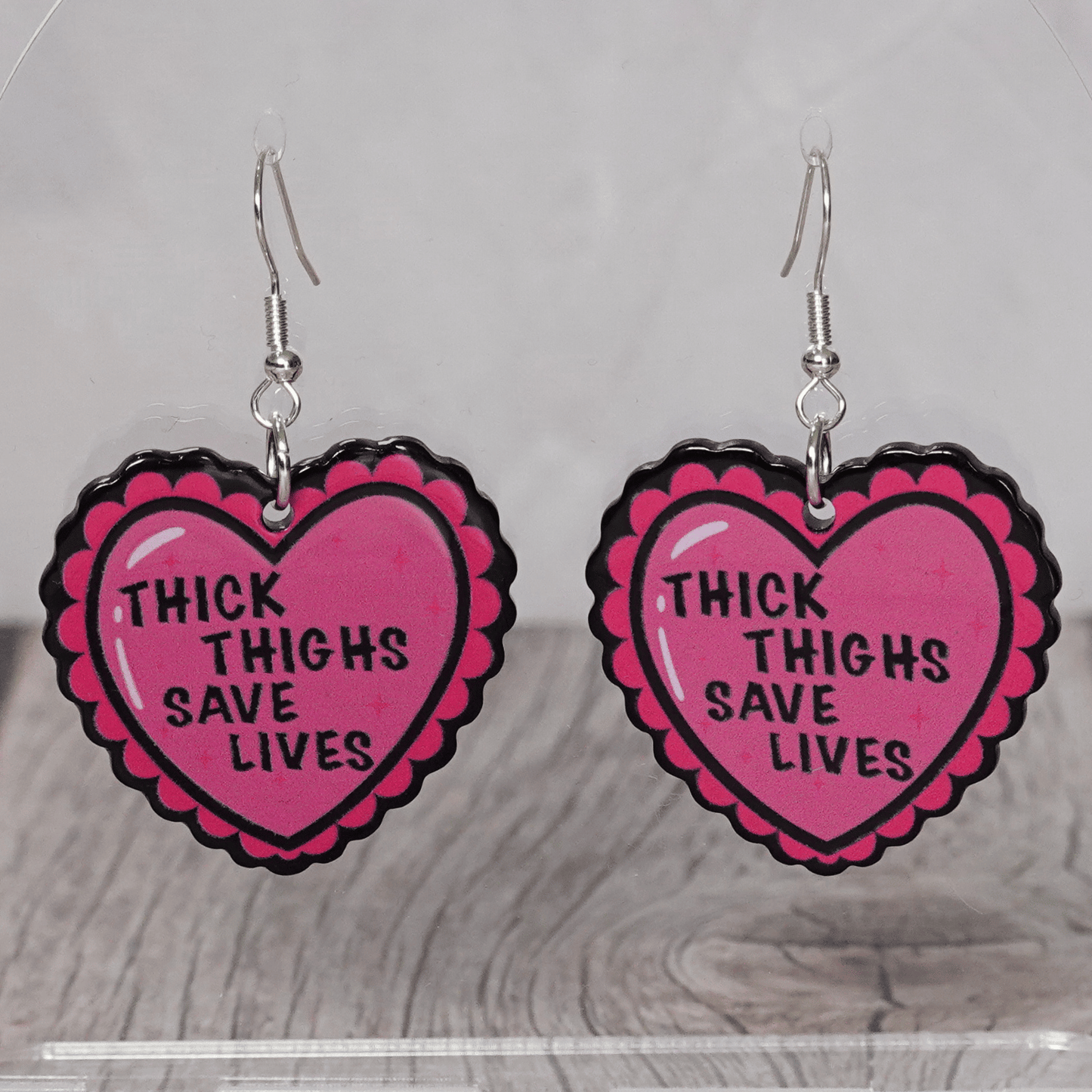 Pink heart dangle earrings with text “thick thighs save lives”