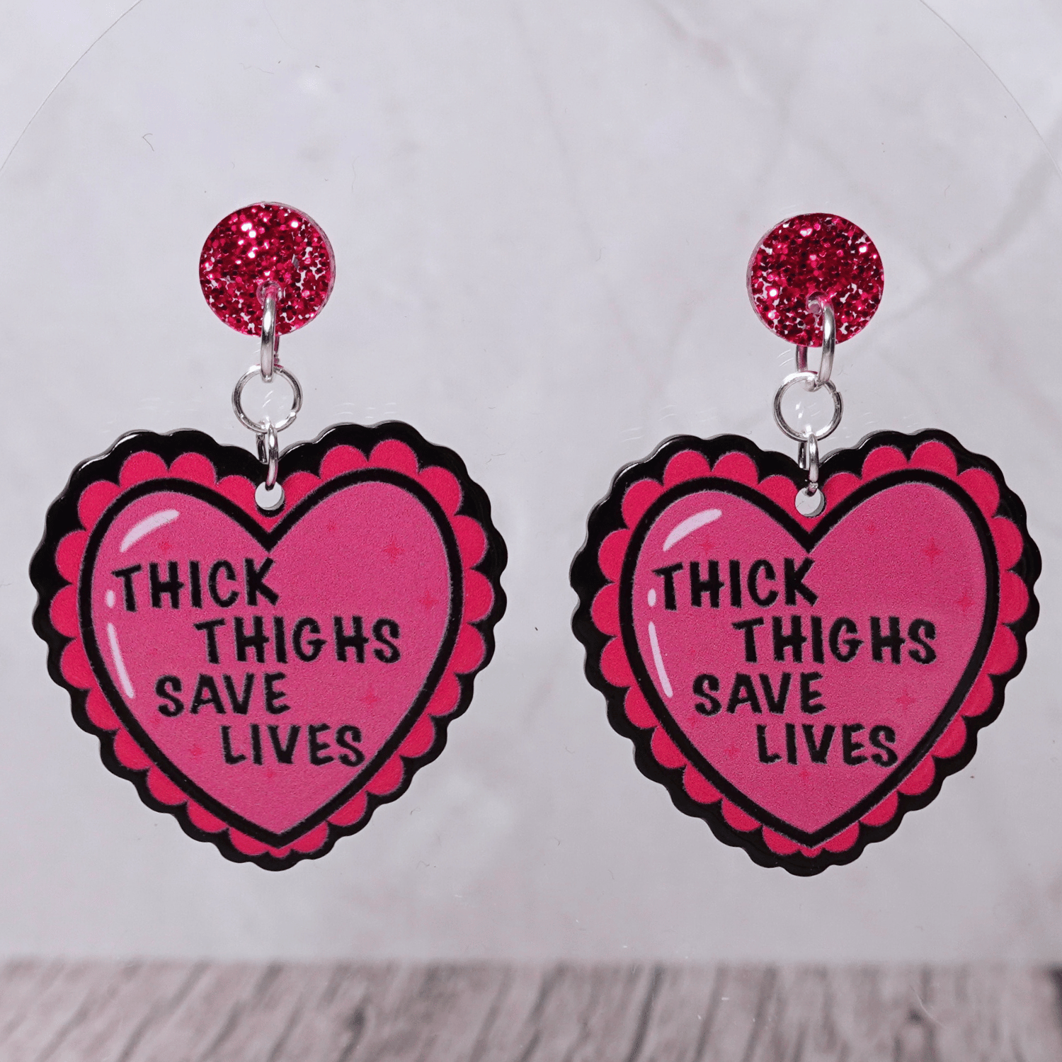 Pink heart dangle earrings with text “thick thighs save lives” and glitter stud tops