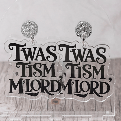 Clear acrylic dangle earrings with black text reading “‘Twas the tism, m’lord” in decorative lettering