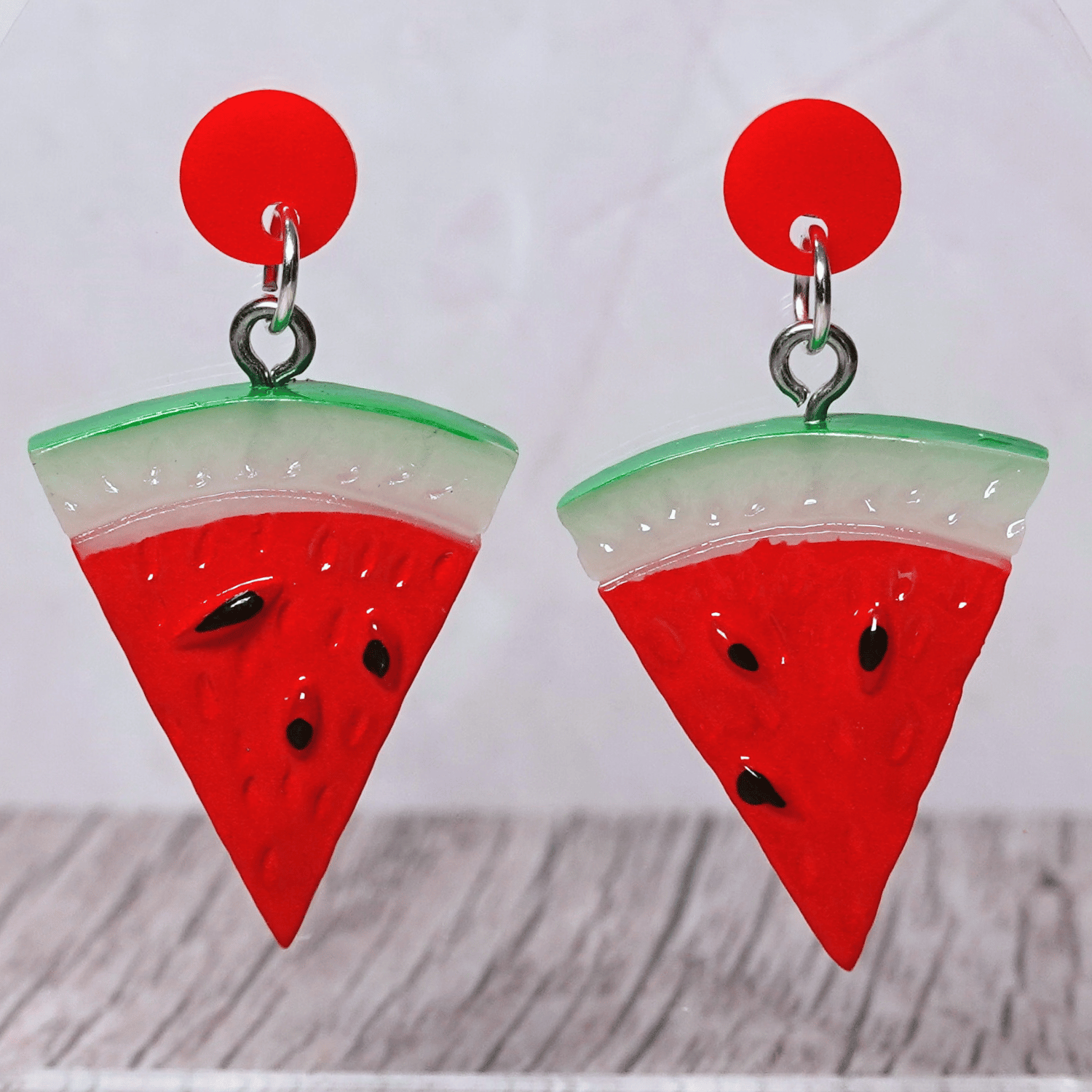 Watermelon slice dangle earrings shaped like red triangular watermelon pieces with green rind and black seed details on red stud tops