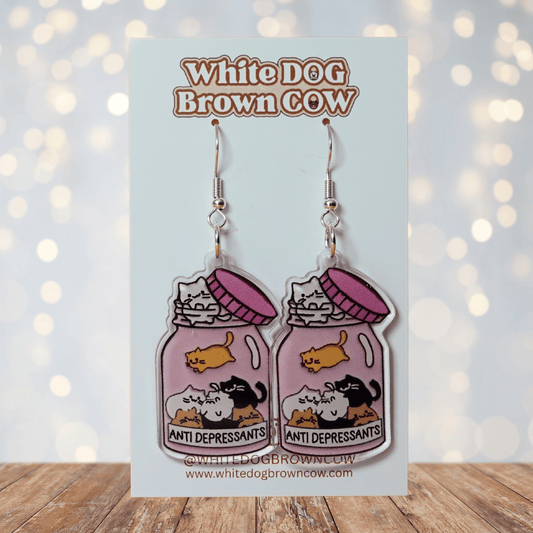 Acrylic dangle earrings shaped like a pink jar labeled “anti-depressants” filled with cartoon cats.