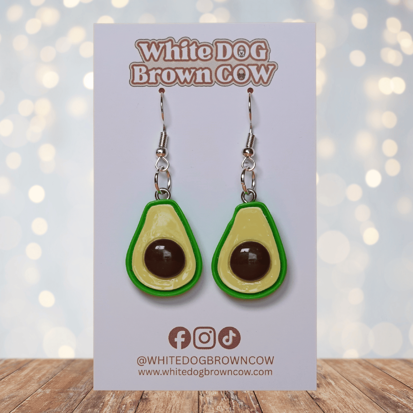 Avocado shaped dangle earrings with green outline, pale yellow center and raised brown pit on silver hooks.