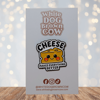 Enamel pin shaped like a smiling yellow cheese wedge with rosy cheeks and the text ‘CHEESE MAKES EVERYTHING BETTER’ on a white background
