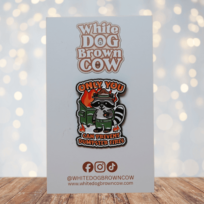 Funny raccoon enamel pin with burning dumpster design and quote “Only You Can Prevent Dumpster Fires,” sarcastic dark humor lapel pin.