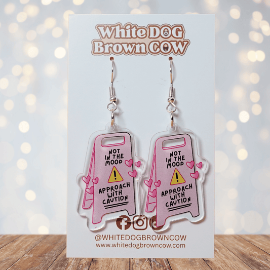 Funny acrylic dangle earrings shaped like a caution sign that reads “Not in the mood – approach with caution,” decorated with small pink hearts.