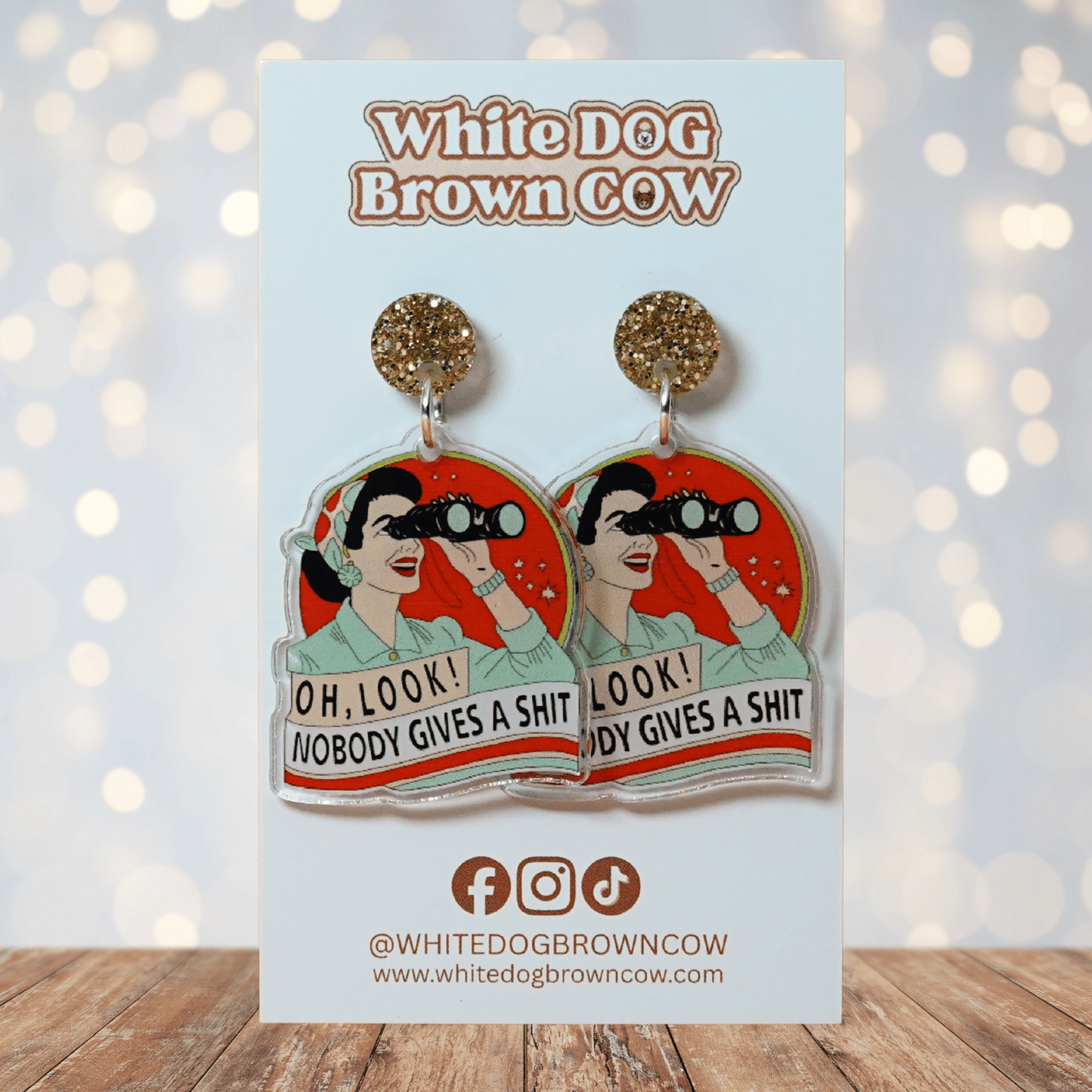 Retro style novelty dangle earrings showing a woman with binoculars and the phrase “Oh look nobody gives a sh*t”