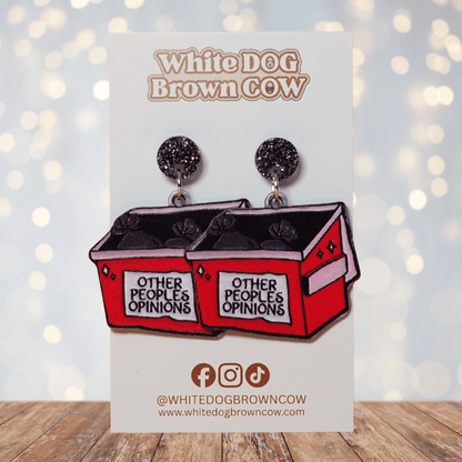 Acrylic dangle earrings shaped like a red dumpster labeled “Other People’s Opinions” with trash bags inside