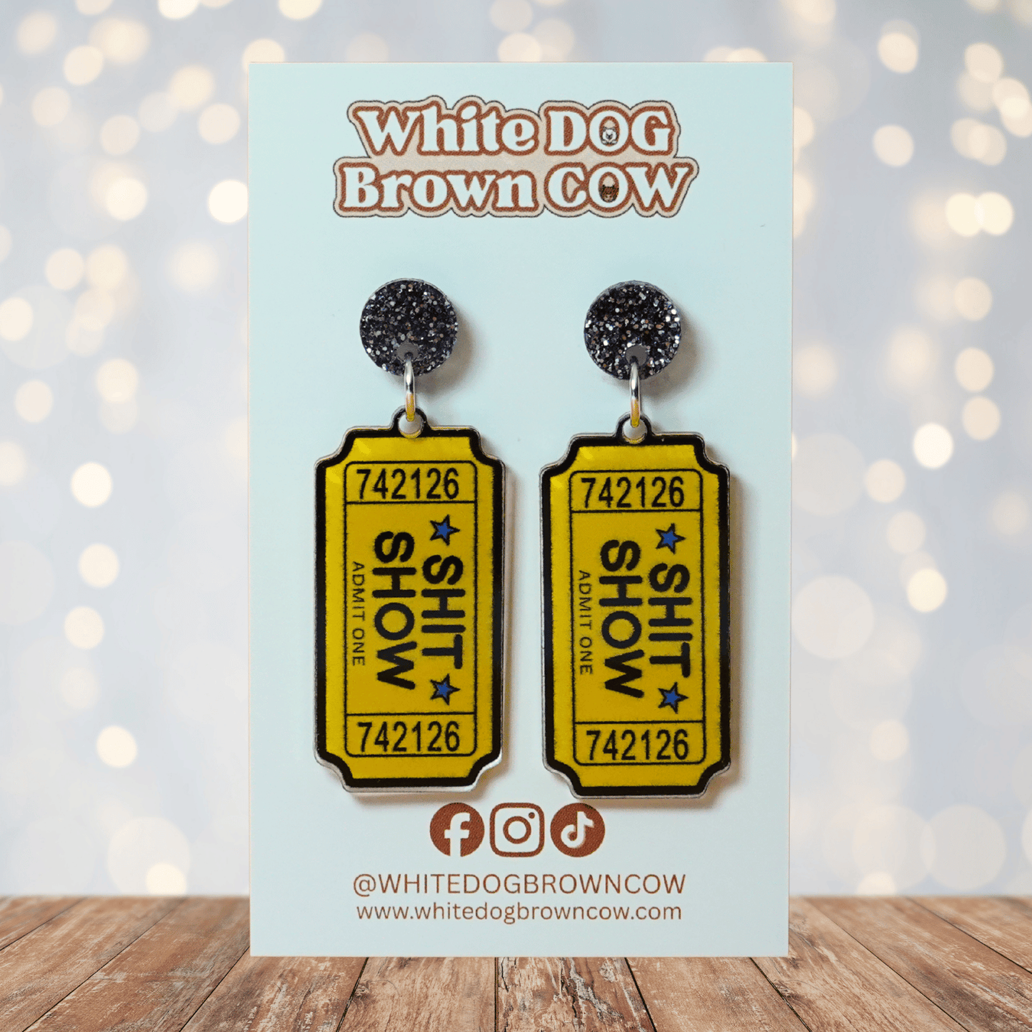 Acrylic dangle earrings designed like yellow admit-one tickets reading “Shit Show”
