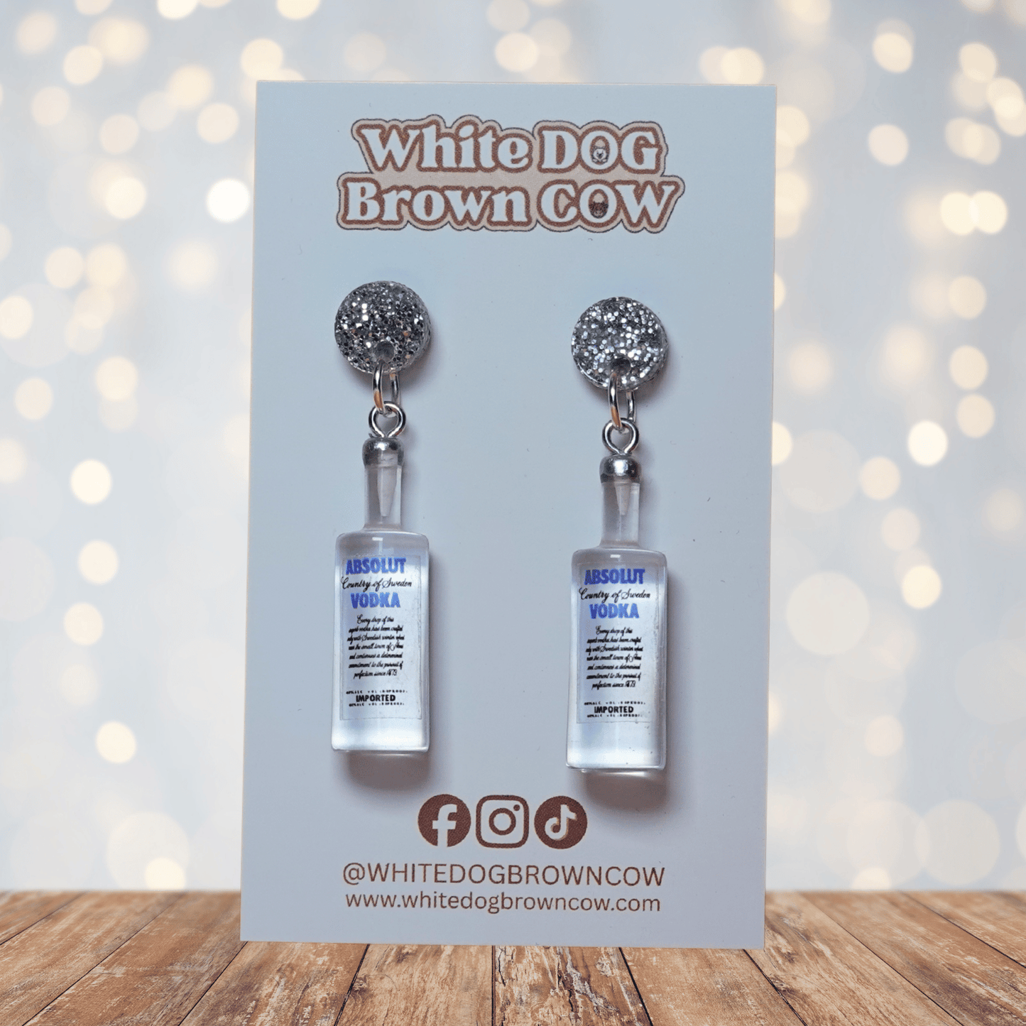 Novelty dangle earrings shaped like clear vodka bottles with a printed vodka-style label design.