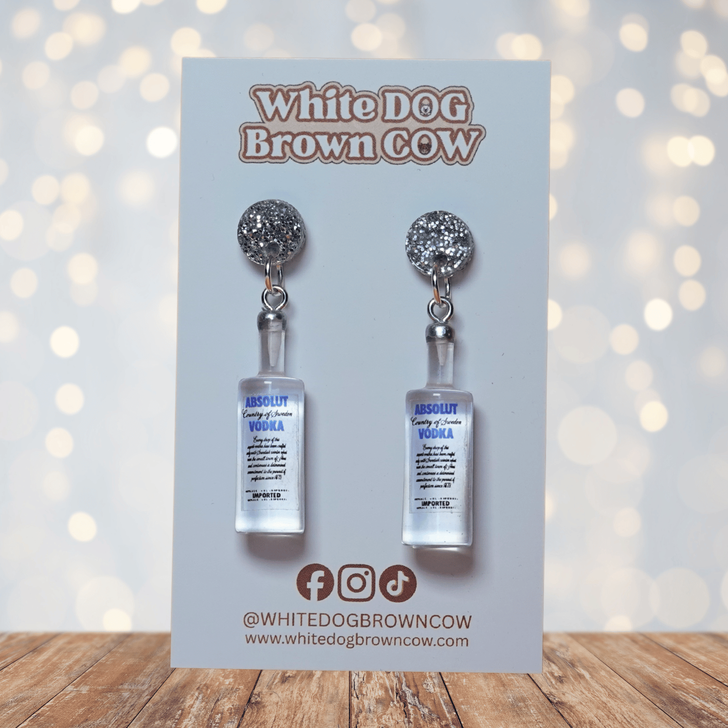 Novelty dangle earrings shaped like clear vodka bottles with a printed vodka-style label design.