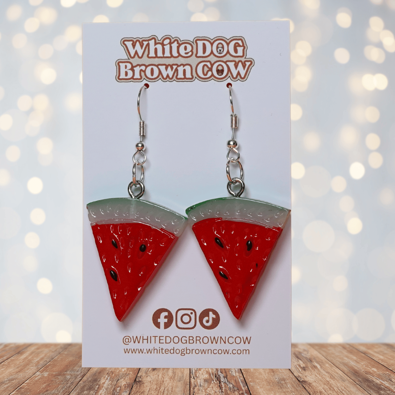 Watermelon slice dangle earrings shaped like red triangular watermelon pieces with green rind and black seed details on silver hooks.